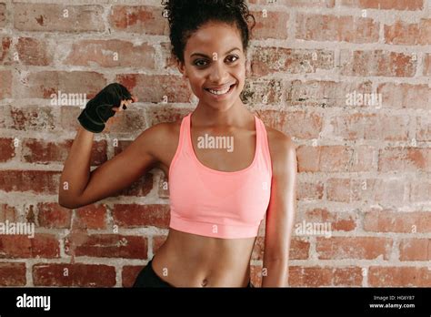 Portrait Of Young Fitness Woman Flexing Muscles And Smiling Against Brick Wall African Female