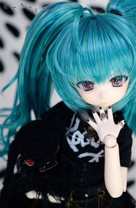 A Doll With Blue Hair Is Holding Her Hand Up To Her Mouth And Looking At The Camera