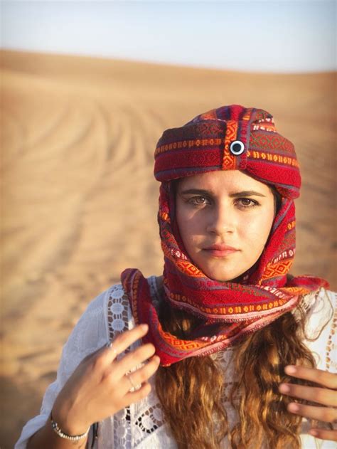 a woman wearing a red hat and scarf in the desert with her hands on her hips
