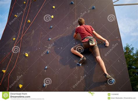Sporty Man Practicing Rock Climbing In Gym On Artificial Rock Training Wall Outdoors Young