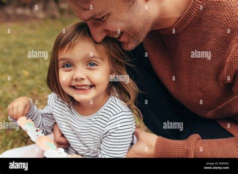 Lächelnde Mädchen sitzen mit ihrem Vater im Freien mit einem Zucker
