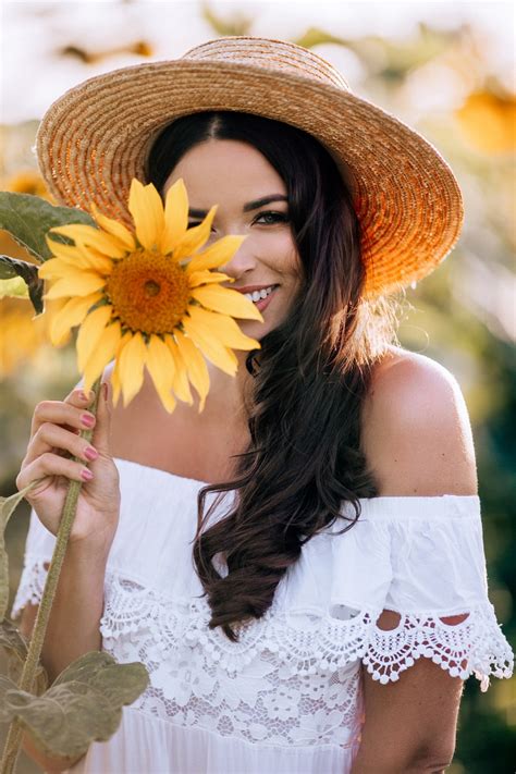 A Woman Wearing A Straw Hat Holding A Sunflower