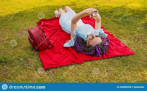 Young Woman Lying On A Blanket Blowing Uses A Smartphone In The Park