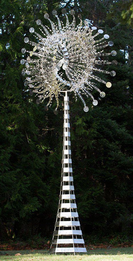 A Tall Metal Sculpture With Lots Of Balls On Its Side In Front Of Some