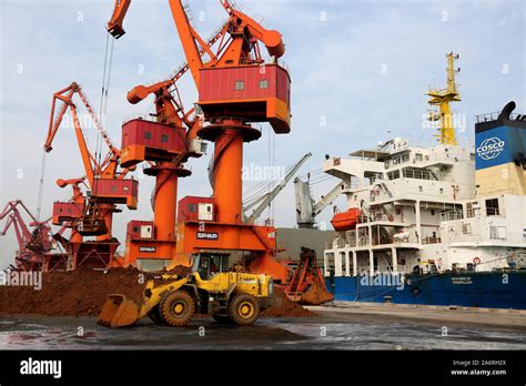 Grab Bucket Cranes Along A Quay Unload Iron Ore From A Bulk Cargo Ship
