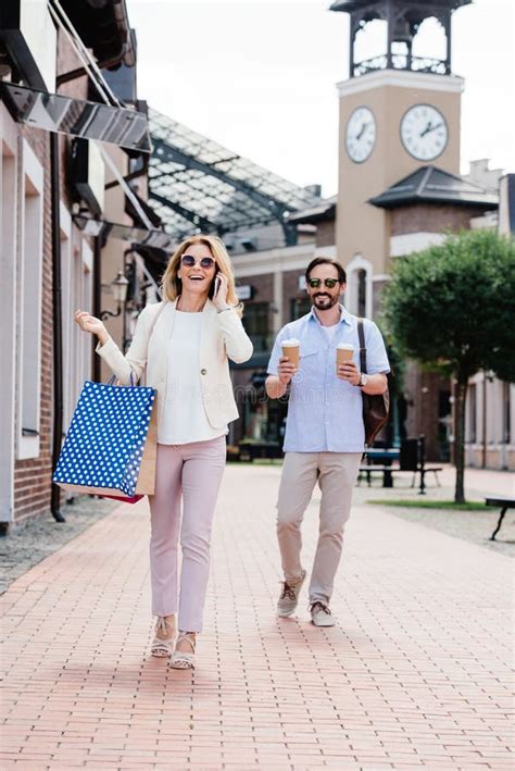 Wife Talking By Smartphone And Holding Shopping Bags Husband Carrying Disposable Coffee Cups