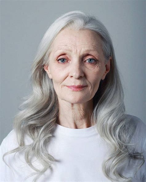 An Older Woman With Grey Hair And Blue Eyes Wearing A White T Shirt Looking At The Camera