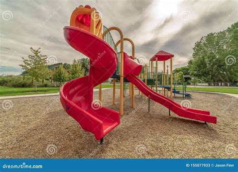 Playground With Bright Red Slides Against Trees And Cloudy Sky
