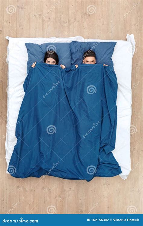 Bedtime Young Couple Lying On Bed Hiding Under Blanket Top View Looking Camera Playful Stock