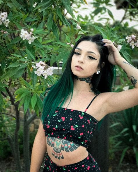 A Woman With Green Hair And Tattoos Standing In Front Of A Tree Wearing