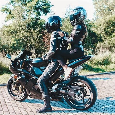 Two People Sitting On The Back Of A Motorcycle Wearing Helmets And