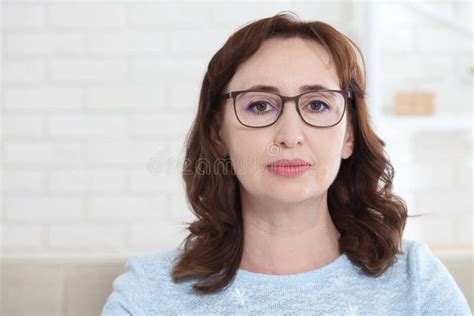 A Middle Aged Woman Wearing Glasses Looks Kindly At The Camera While Sitting At Home On The