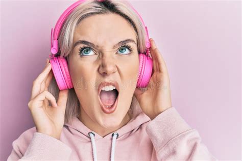 Young Blonde Girl Listening To Music Using Headphones Angry And Mad