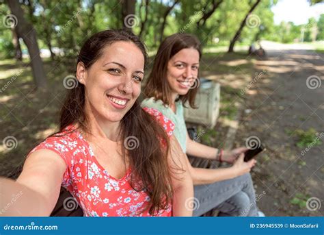 Girlfriends Taking Selfie Together Having Fun Outdoors Holding Phone Looking At Camera Directly