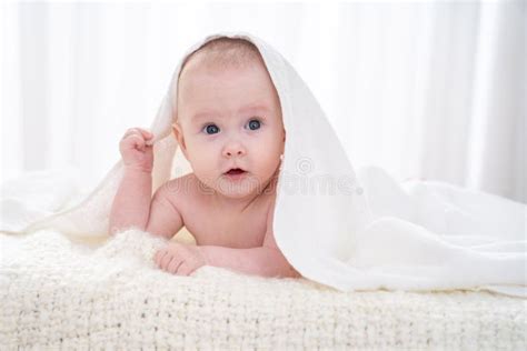 Charming Sweet Baby Is Lying On Bed Under A White Blanket On A White