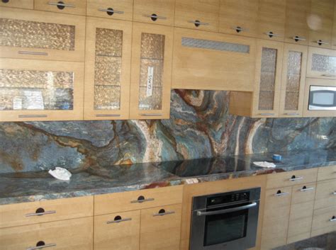 A silver and gold range hood unities with white brick tiles and a swivel swing arm pot filler over a wolf integrated gas cooktop facing an. Blue Louisa | Granite Countertops Seattle