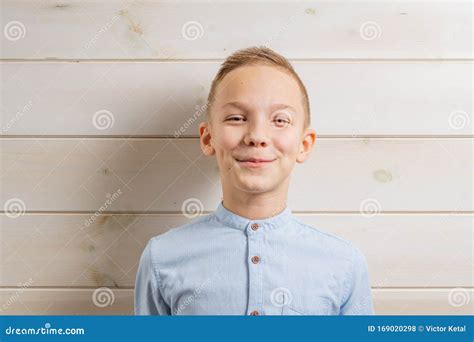 A Boy Of 10 Years Old In A Blue Shirt Smiles On A Light Wooden