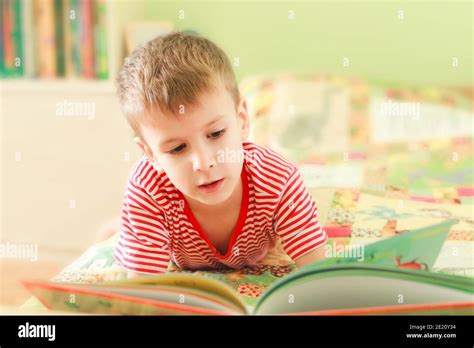 Cute Little Boy Reading Alphabet Book While Laying On Bed Child Looks