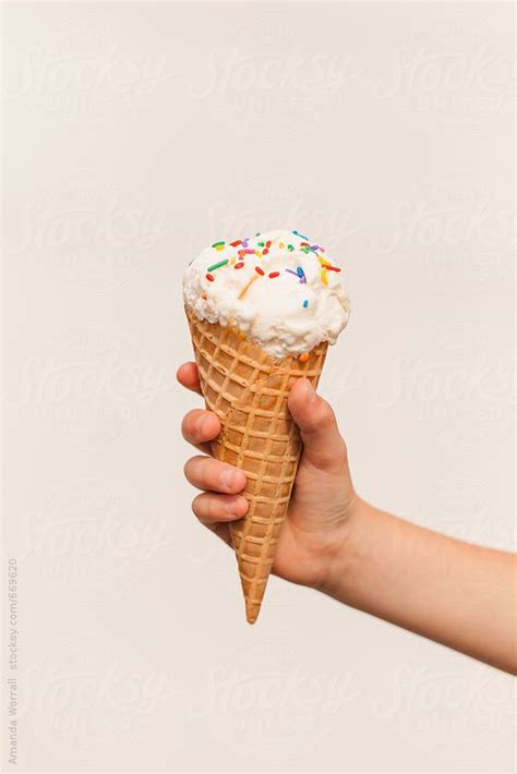 Childs Hand Holding An Ice Cream Cone With Sprinkles Against A White