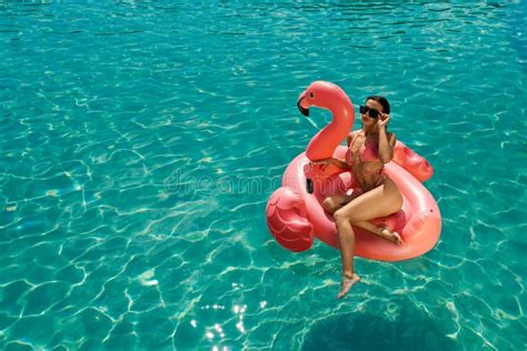 Brunette Girl Swimming In Pool Sitting On Pink Flamingo Stock Image