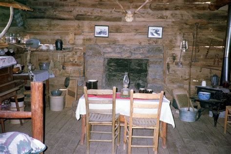 An Old Log Cabin Dining Room With Chairs And Table In Front Of The Fire