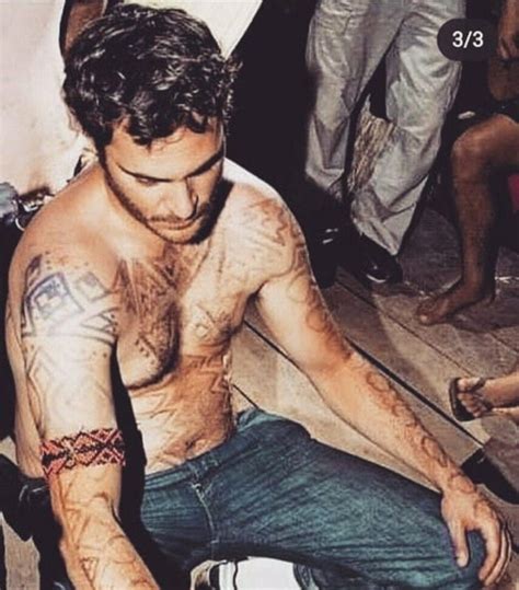 A Man Sitting On The Ground With Tattoos On His Chest And Arm Holding A Knife