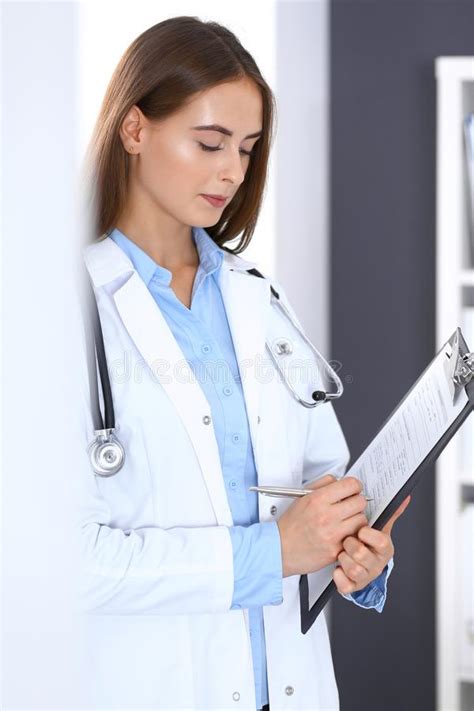 Doctor Woman Filling Up Medical Form While Standing Near Window In