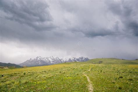 Mountain Peaks With Snow And Green Pastures Under Dark Cloudy Sky In