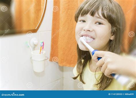 Girl Brushing Her Teeth With Toothpaste Smiles And Looks Into The Lens