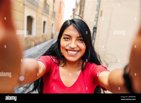 close up selfie of brunette latin girl smiling holding the camera with both hands on a european
