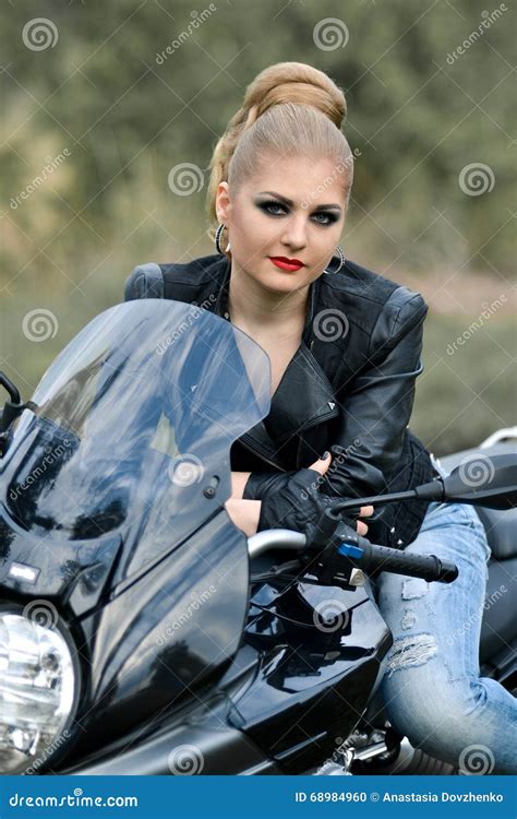 Serious Blonde Girl Sit On Black Biker With Leather Jacket Stock Photo
