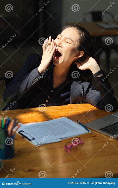 Sleepy Asian Business Woman Yawning At Her Office Desk Stock Photo