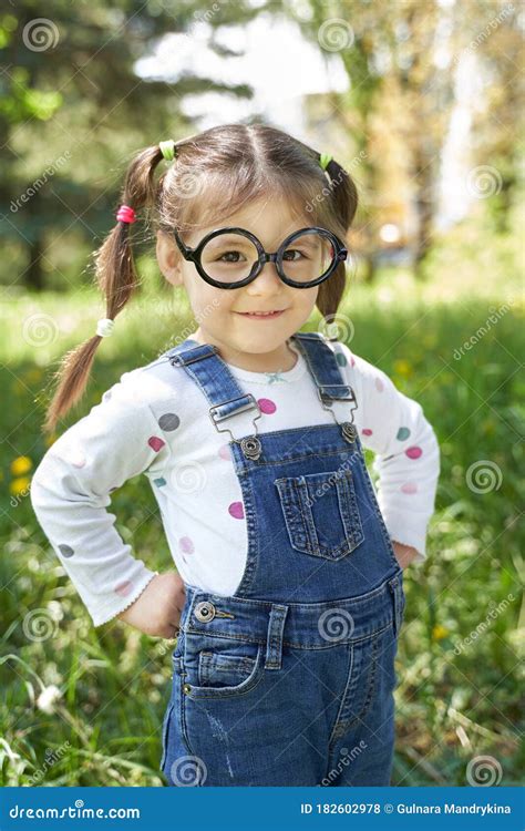 A Healthy Girl With Two Pigtails And Glasses Stands With Her Hands On