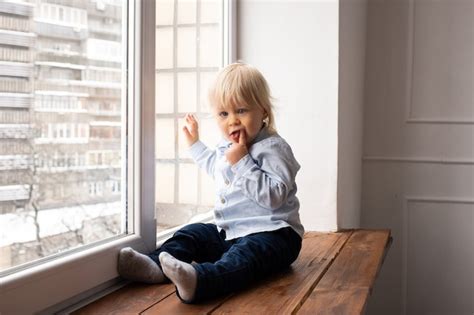 Le Petit Garçon Se Tient Près Du Rebord De La Fenêtre Photo Gratuite