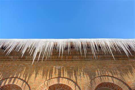 Big Icicles On The Roof Of A Townhouse On A Snowy Winter Day Among Thaw