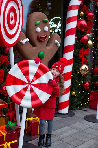 A Sixyearold Blond Girl Dressed In Red Licks A Huge Caramel In Front Of A Christmas Tree With A