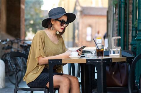 Elegant Italian Woman With Hat And Glasses Checks Her Makeup On Her Smartphone Stock Image