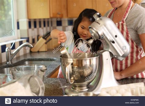 A kitchen has many kitchen utensils that is used for preparing and serving food such as saucepan, knife and grater. Young girl helping mother bake in kitchen Stock Photo ...