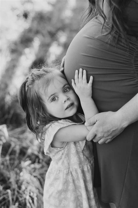 A Black And White Photo Of A Pregnant Woman Hugging Her Daughter