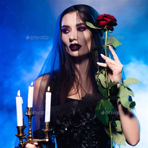 Woman In Black Dress And Veil Holding Red Rose And Burning Candles On