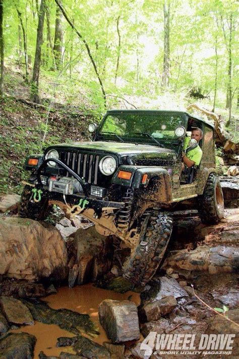A Man Driving A Jeep Through Some Muddy Water In The Woods With Rocks