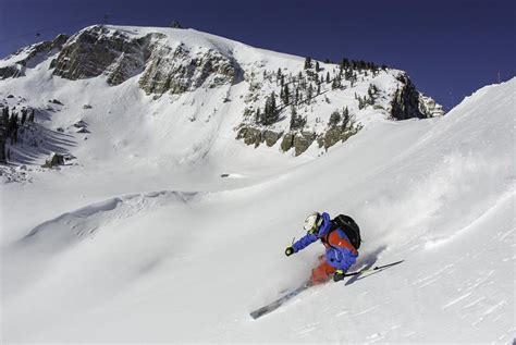 A Man Riding Skis Down The Side Of A Snow Covered Slope In Front Of A