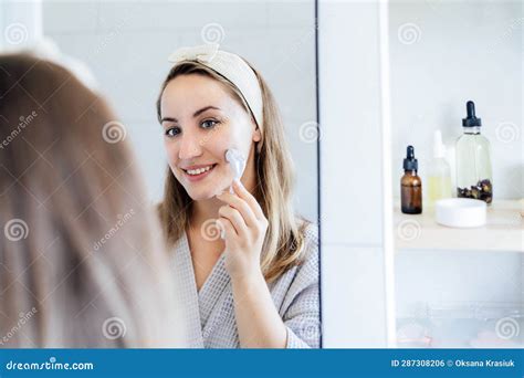 Young Woman In Bathrobe Looking In Mirror And Making Face Massage With Micro Needle Meso Derma