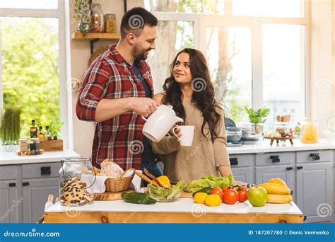 Beautiful Young Couple Is Talking Smiling While Eating Tea Or Coffee And Drinking In Kitchen At