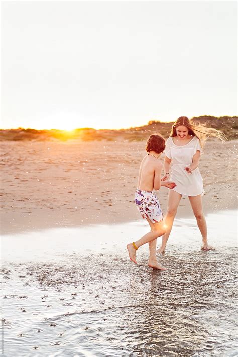Girl And Boy Splashing And Having Fun Together At The Beach At Sunset