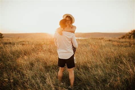 A Man With A Woman In A Hat Hug And Kiss In The Tall Grass In The Meadow Stock Image Image Of