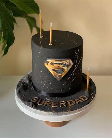 A Black Cake With A Gold Superman Symbol On Top And Candles Sticking