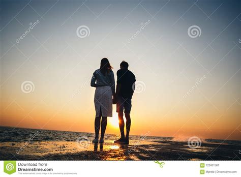 Silhouette Of Couple Standing At The Pier Watching The Sunrise At The