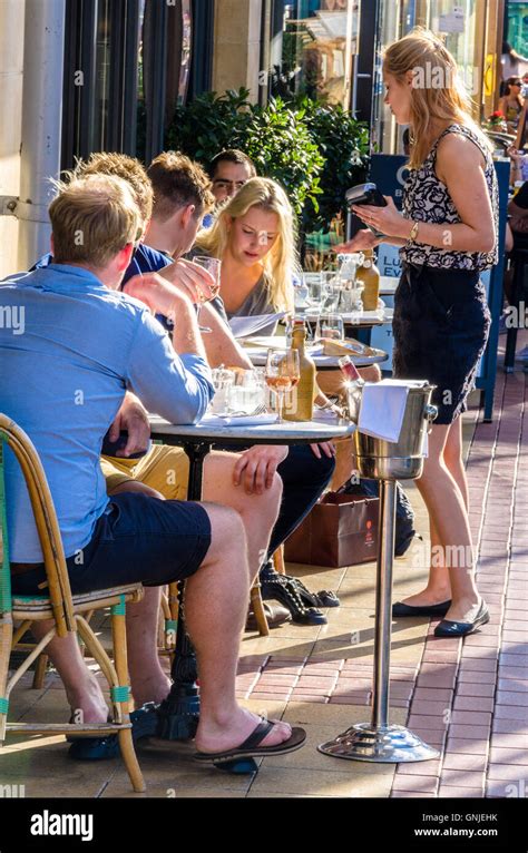People Sit And Enjoy A Meal Outside As A Waitress Takes Payment Using A