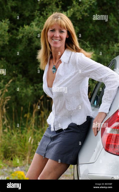 Mature Woman Wearing A White Shirt And Skirt Leaning On A Car Stock